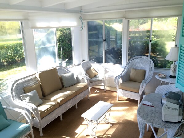 A sunlit room with wicker furniture, large windows, and a small table with a printer.