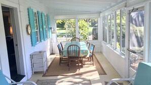 Une terrasse couverte avec une table et des chaises, une vue sur l’extérieur et une porte donnant sur une autre pièce.