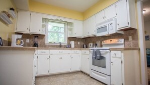 Una cocina con armarios blancos, microondas, horno y cafetera.