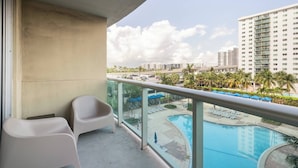 A balcony with a view of a swimming pool, palm trees, and high-rise buildings. - Beautiful 1 bedroom apartment fully furnished steps away from the beach (Sunny Isles Beach)