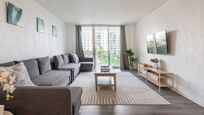 A modern living room with a grey sofa, a coffee table, and a TV on the wall. - Beautiful 1 bedroom apartment fully furnished steps away from the beach (Sunny Isles Beach)