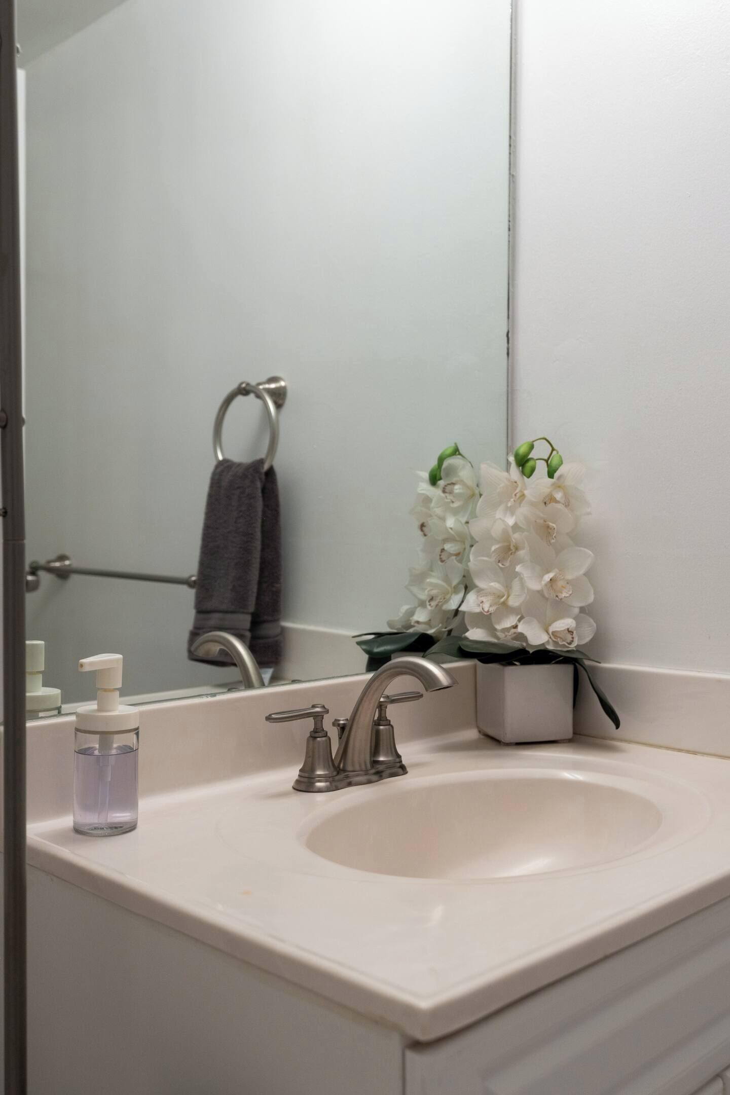 A bathroom with a white sink, a mirror, a towel ring, and a small orchid arrangement.