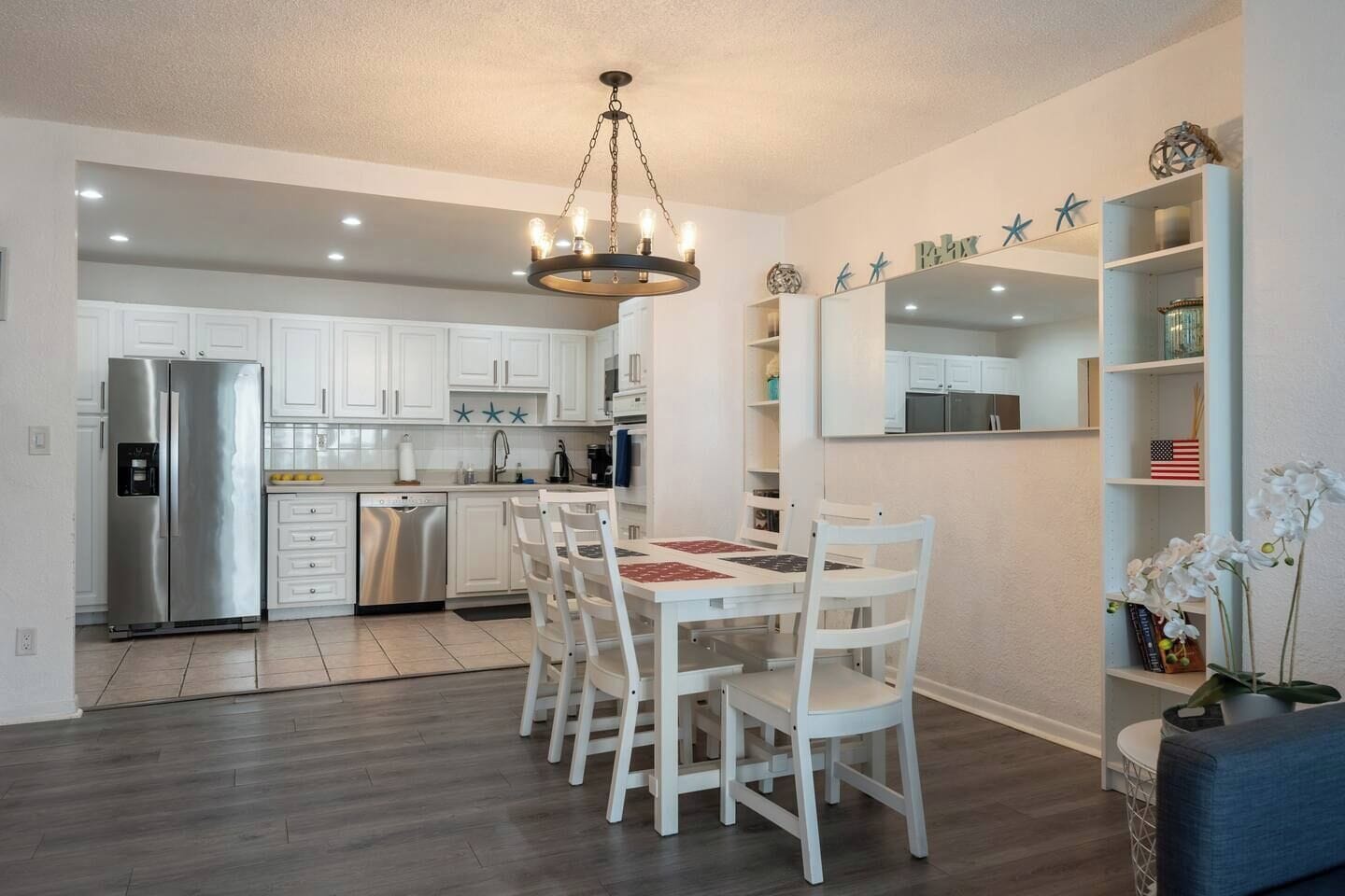 Une cuisine moderne avec des meubles blancs, un réfrigérateur en acier inoxydable et un coin repas comprenant des chaises et une table, le tout dans des tons blancs.