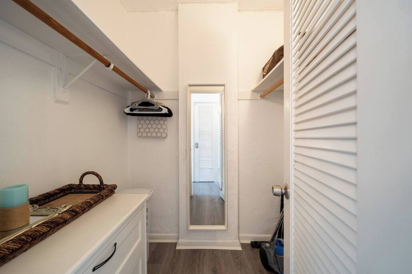 A narrow hallway with a door leading to a room, a small shelf with a bag, and a trash bin.