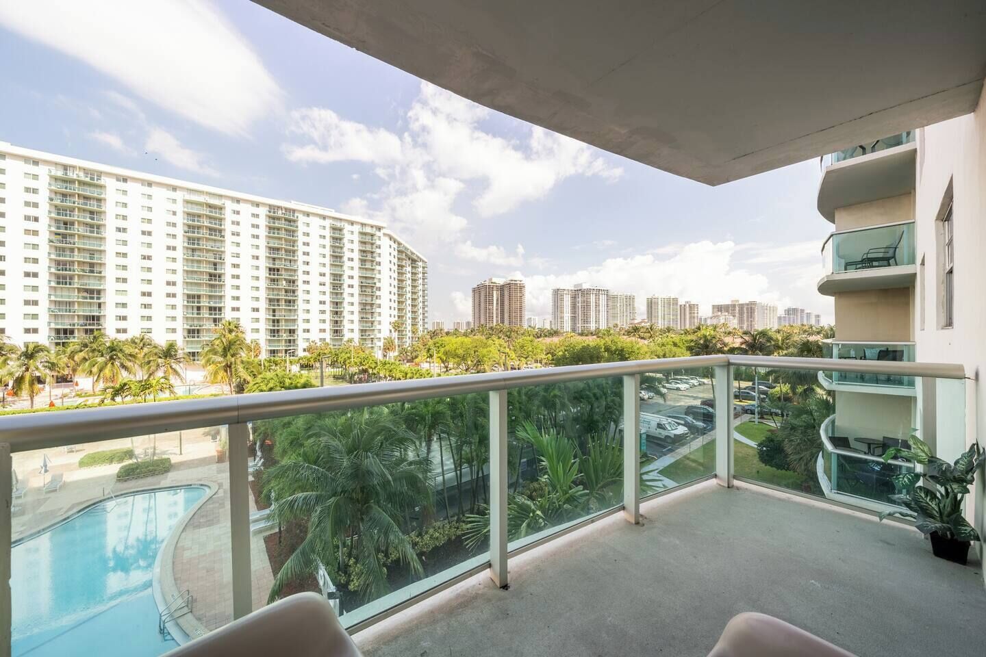 Uma varanda com vista para uma piscina, palmeiras e edifícios altos.