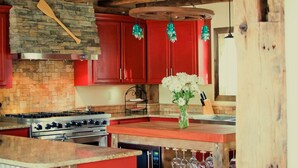 Una cocina rústica con vigas de madera, armarios rojos y salpicadero de piedra.