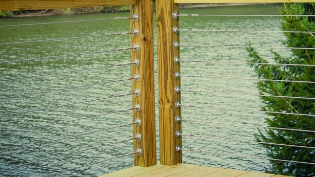 Una terraza de madera con barandillas metálicas que da a un cuerpo de agua tranquilo, rodeada de abundante follaje verde.