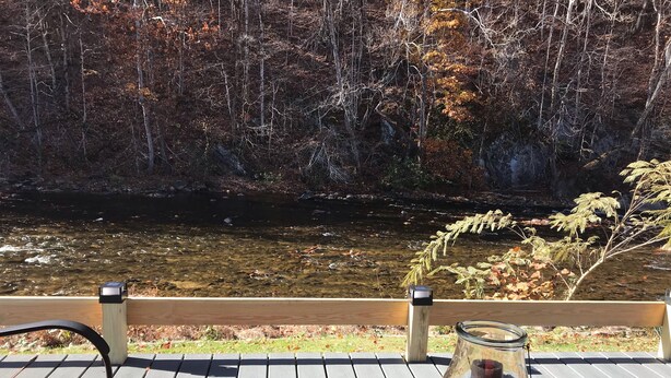 Un terrazzo in legno con tavolo e sedie che si affaccia su un fiume e il foliage autunnale.
