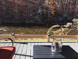 A wooden deck with a table and chairs overlooking a river and autumn foliage.