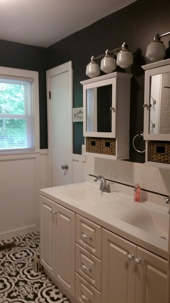 A bathroom with a white vanity, a large mirror, and a window with blinds.
