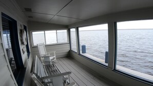 Una terraza con un banco y una silla, ventanas amplias con vista al agua y un flotador en la pared.