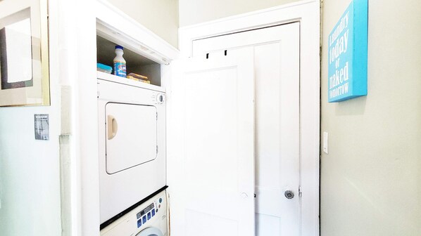 A laundry room with stacked washers and dryers, a door, and a sign on the wall.