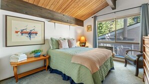 A bedroom with a bed, bedside table, lamp, and a window with a view of the outside. - Raccoon Roost Condo | Community Pool & Club House (Incline Village)