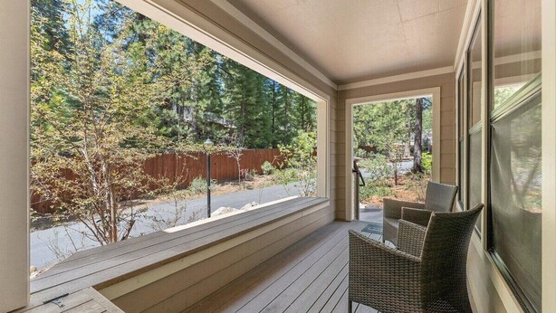 A covered porch with a view of a wooded area, a wooden bench, and wicker chairs. - Raccoon Roost Condo | Community Pool & Club House (Incline Village)