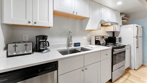 A modern kitchen with white cabinets, a built-in dishwasher, a stove, and a microwave. - Raccoon Roost Condo | Community Pool & Club House (Incline Village)