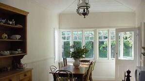 Un comedor con mesa y sillas de madera, una araña y ventanas amplias con vista a zonas verdes.