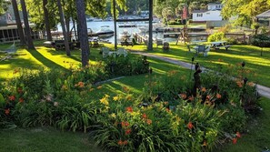 Un jardín bien cuidado con diversas flores y árboles, un área de picnic y vistas a barcos en el agua.