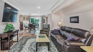 Ein Wohnzimmer mit einem braunen Ledersofa, einem Flachbildfernseher, einem Holztisch und einem gemusterten Teppich.