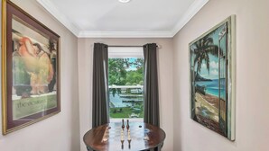 Ein Zimmer mit Schachbrett, gerahmten Bildern und Blick auf Garten und Wasserfläche.