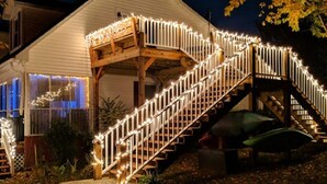 Ein weißes Gebäude mit einer Holztreppe und -geländern, verziert mit Lichterketten, vor einem Nachthimmel mit Mond.