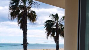 A balcony with a table and chairs, overlooking a beach with palm trees and the ocean. - Large apartment. Front line beach, private parking, bicycles (Peñiscola)