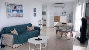 A modern living room with a teal sofa, a white coffee table, and a dining area with a wooden table and chairs. - Large apartment. Front line beach, private parking, bicycles (Peñiscola)