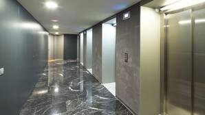 A modern hallway with a marble floor, elevators, and a plain wall with a light switch. - Two bedroom apartment with terrace - You Stylish (Barcelona)