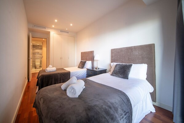 Une chambre d’hôtel avec deux lits, une armoire, une table de chevet et une salle de bain visible à travers une porte ouverte.