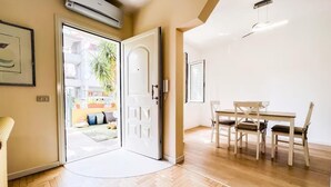 A room with a wooden herringbone floor, a white door leading to a balcony, and a dining area with a table and chairs.