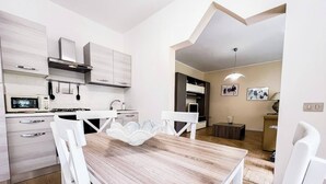 A modern kitchen with white cabinetry, a microwave, and a dining area with a wooden table and white chairs.