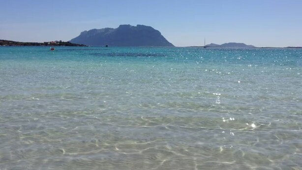 A clear coastal view with a prominent mountain in the background.
