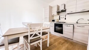 A modern kitchen with white cabinetry, a wooden dining table, and a black oven.