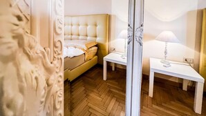 A hotel room with a tufted headboard bed, two bedside tables with lamps, and a herringbone-patterned wooden floor.