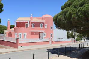 A pink building with a white fence, a road in front, and a large tree to the right. - Luxury Villa with swimming pool (Falésia)
