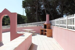 An outdoor patio area with a pink wall, white fence, and a brick barbecue grill. - Luxury Villa with swimming pool (Falésia)