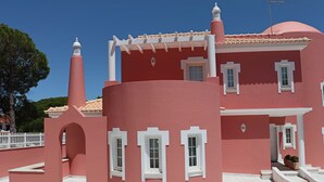 Un edificio rosa con detalles blancos, techo de tejas y cerca blanca.