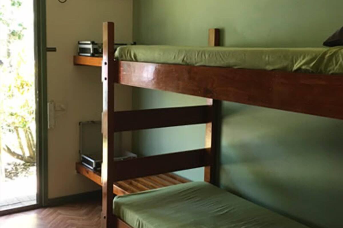 Una cama litera con un colchón verde, cabecera de madera y un pequeño estante sobre la cama inferior.