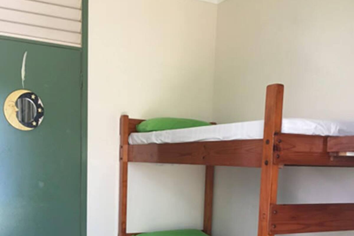 Una cama litera con almohadas verdes en una habitación con suelo de madera con patrón de espiga y una puerta verde.