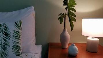 A bedroom with a bed, a nightstand with a lamp, a small vase, and a potted plant.