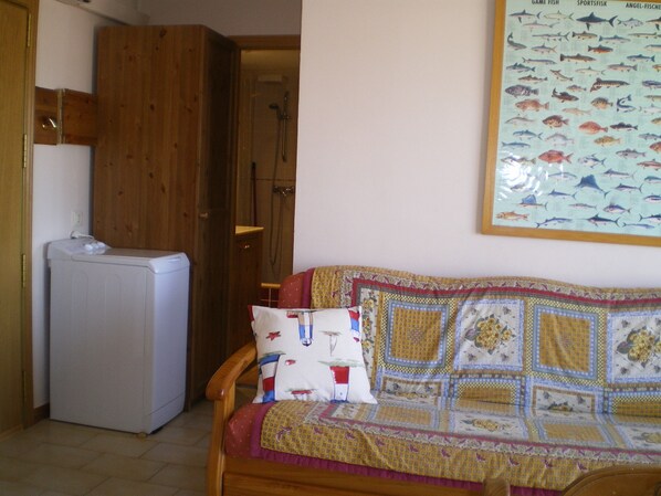 Una habitación con un armario de madera, una lavadora blanca, un sofá estampado y una pared con una ilustración de peces.