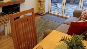 Een woonkamer met een houten eettafel, een bank, een aan de muur bevestigde televisie en een schuifdeur naar een buitenruimte.