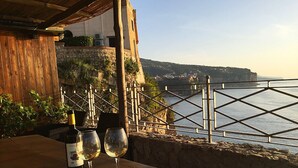 A wooden table with two wine glasses and a bottle, overlooking a coastal view with a stone wall and metal railing. - Villa Bikini, a paradise on the rock steep above the sea with swimming pool. (Napoli)