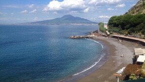 A coastal view with a beach, a mountain in the background, and a clear sky. - Villa Bikini, a paradise on the rock steep above the sea with swimming pool. (Napoli)