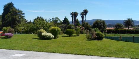 A well-maintained garden with various shrubs and trees, a clear sky, and a distant view of hills.