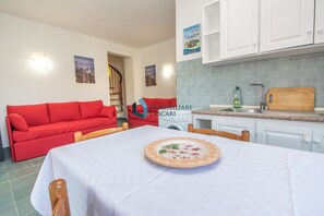 A compact living space with a red sofa, a dining table with a floral plate, a kitchen with a sink and a wooden cutting board, and a washing machine.