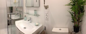 Ein Badezimmer mit einem weißen Waschbecken, einer Toilette und einer Glasablage für Toilettenartikel.