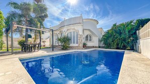 Ein Pool mit Pergola und Sitzgelegenheiten im Freien, umgeben von Palmen und einem weißen Gebäude mit Bogenfenstern.