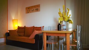 Un salon avec un canapé, une table à manger et des chaises. On peut voir une bouteille et un verre sur la table.
