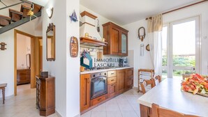 A kitchen with wooden cabinets, a stove, and a dining area with a table and chairs. - Villa Limuti with shared swimming pool (Cefalù)