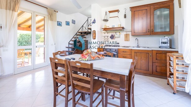 A spacious kitchen with wooden cabinets, a dining table, and a staircase leading to an upper level. - Villa Limuti with shared swimming pool (Cefalù)